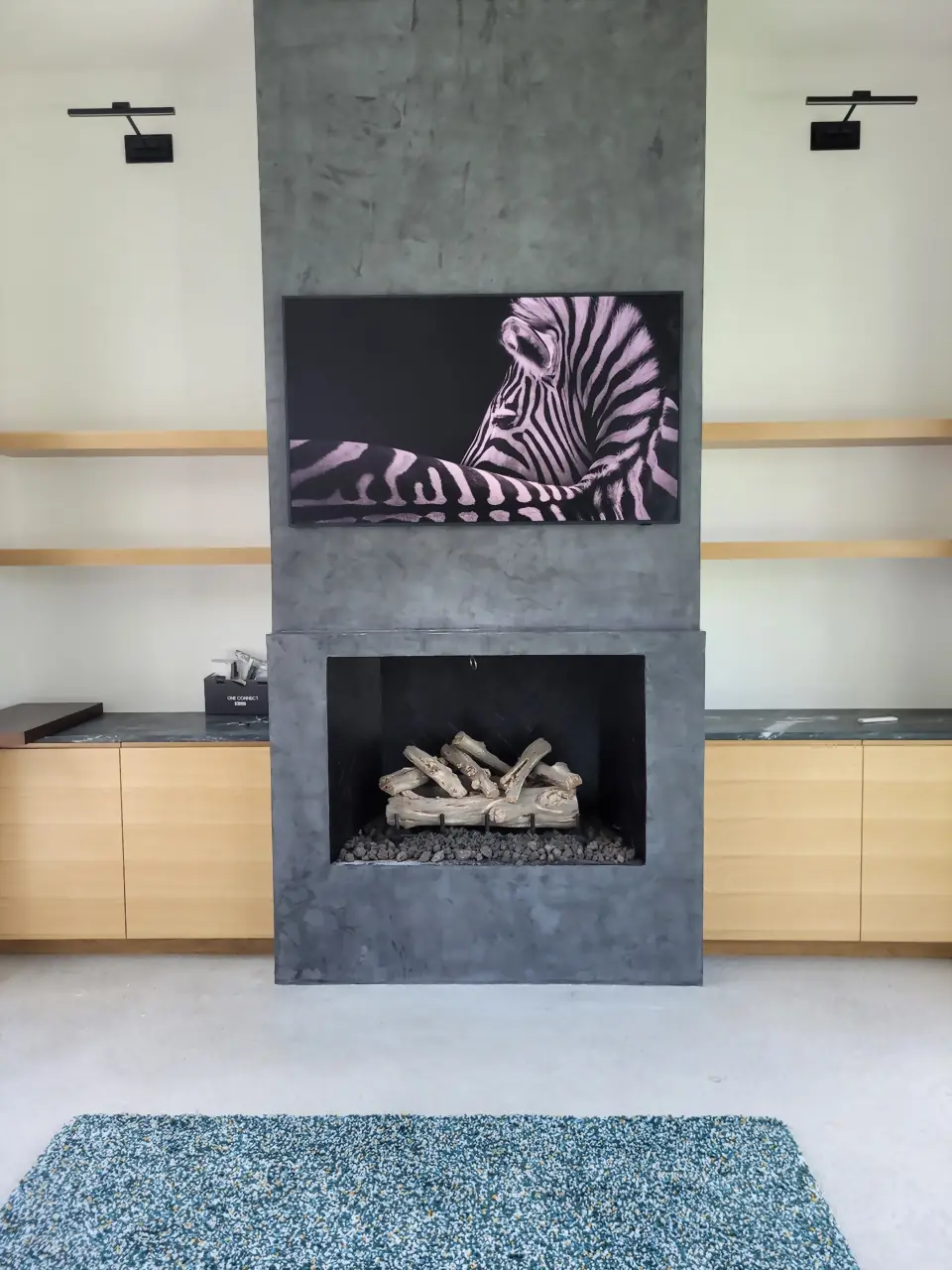 Samsung Frame TV with zebra art on a board-formed concrete fireplace column beside oak built-ins