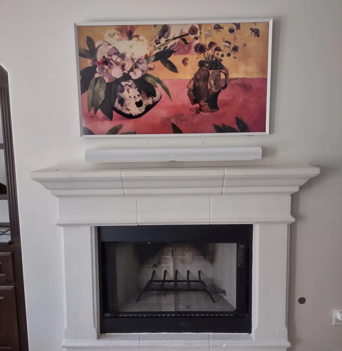 Samsung Frame TV displaying floral still-life art with a white soundbar above a cast mantel