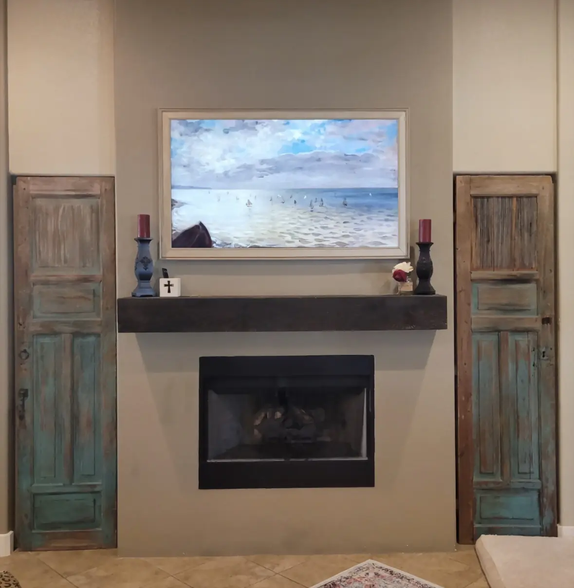 Samsung Frame TV displaying a sailboat painting above a dark beam mantel, flanked by rustic doors