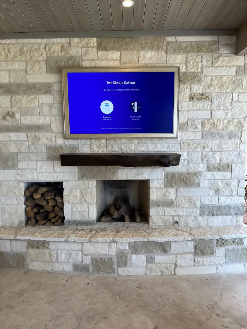 Outdoor white limestone fireplace with a TV above a live-edge wood mantel under a plank ceiling
