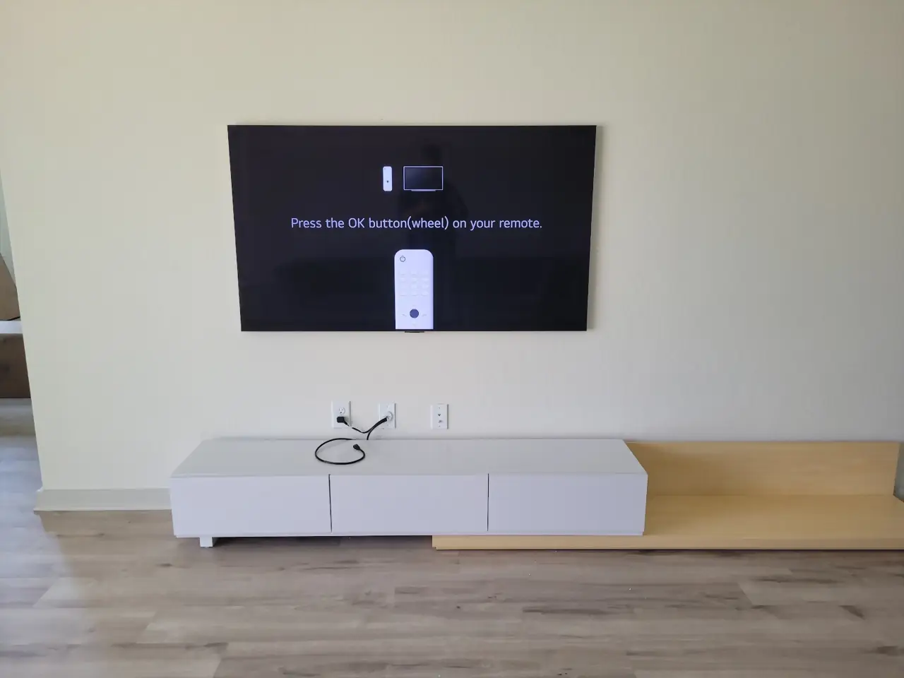 TV mounted level above a low white and wood console in a bright living room