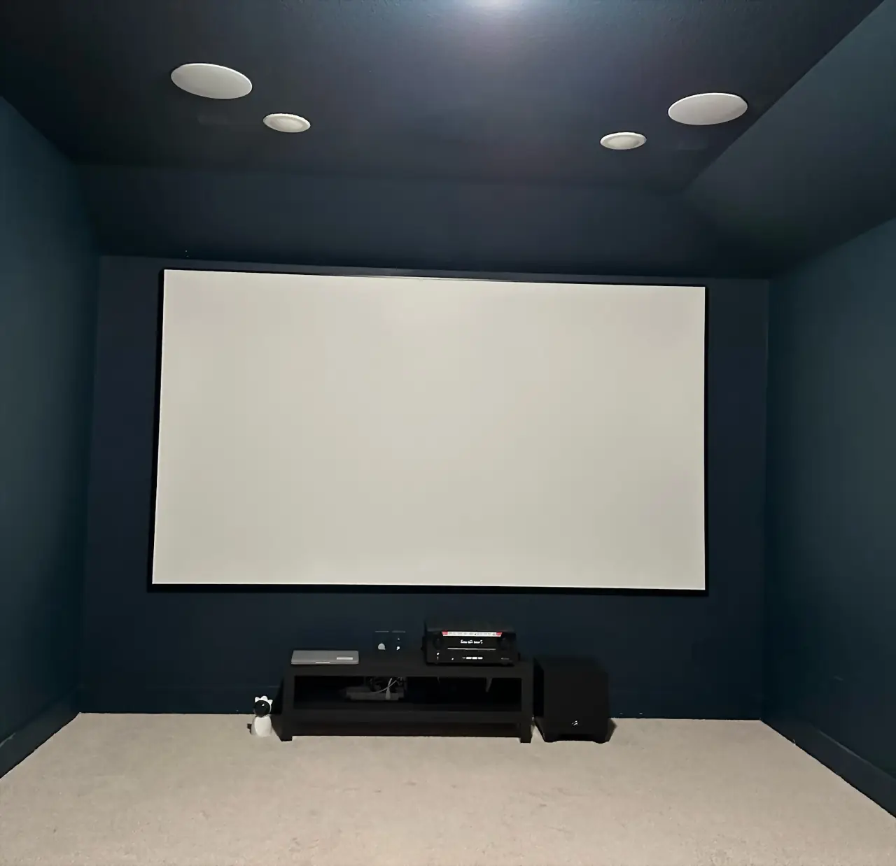 Navy-walled dedicated theater room with projection screen and four in-ceiling speakers