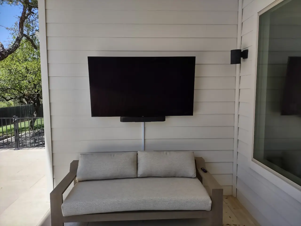 Outdoor TV and soundbar mounted on white lap siding above a covered patio seating area