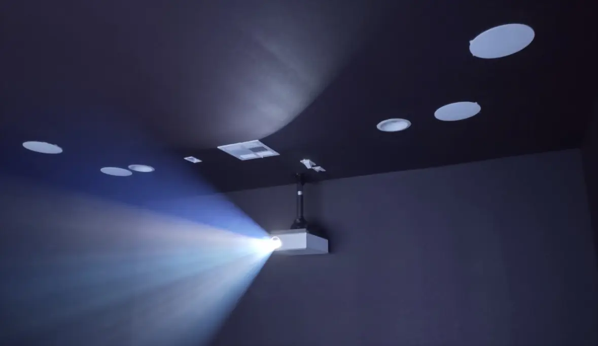 Ceiling-mounted projector beaming in a dark home theater with in-ceiling speakers