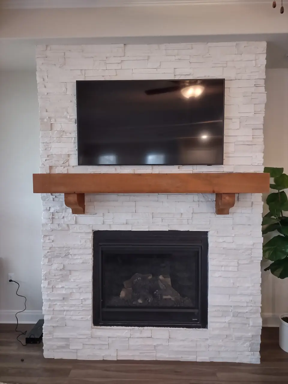White stacked-stone fireplace with a TV mounted above a rough-hewn wood beam mantel on corbels