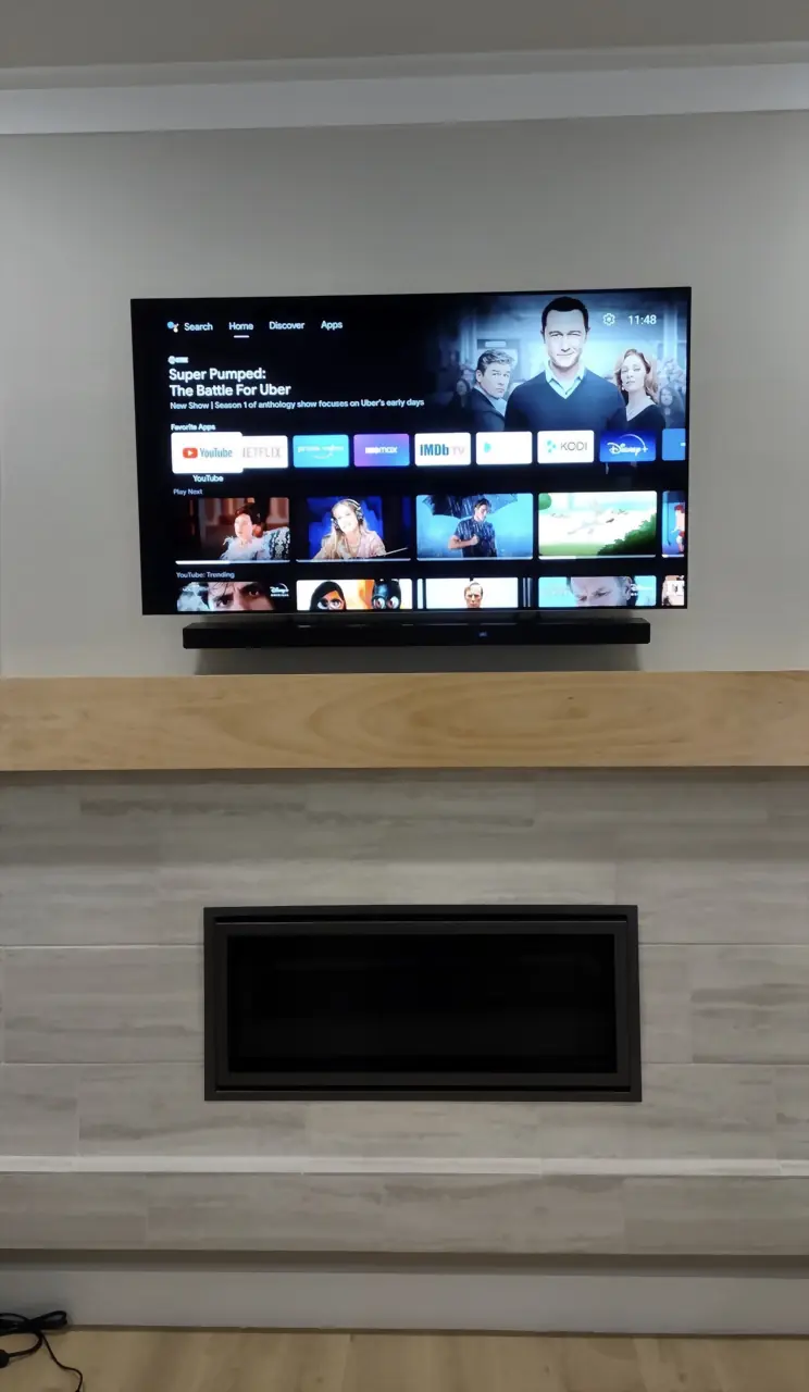 TV and soundbar above a light wood mantel and modern tile fireplace with a linear insert