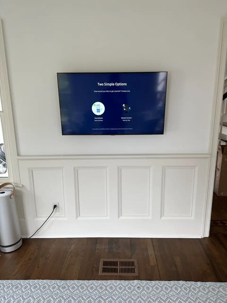 TV mounted on a white wall above wainscoting panels in a new-build living room